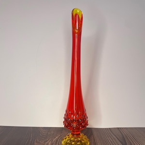 May include: A tall, red and yellow glass vase with a textured, bubbled design. The vase has a narrow neck and a wide base.
