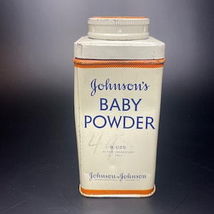 May include: A vintage tin of Johnson's Baby Powder with a white background and blue lettering. The tin is 9 ounces and the active ingredient is talc. The tin is made by Johnson & Johnson and has the locations New Brunswick, N.J. and Chicago, Ill. printed on the bottom.