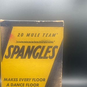 Pode incluir: Uma caixa vintage de cera para piso de dança 20 Mule Team Spangles. A caixa é amarela com letras pretas e uma silhueta de pessoas dançando. O texto diz "Makes every floor a dance floor. Easy to apply - easy to remove."
