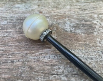 May include: A black hair stick with a white pearl on the top. The pearl is surrounded by a band of small rhinestones.