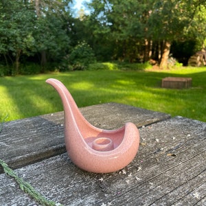 May include: A pink ceramic candle holder shaped like a bird with a textured surface.