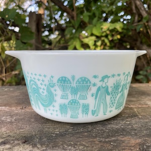 以下が含まれることがあります： 白いパイレックスボウル、ターコイズのデザイン。雄鶏、バスケット、オーバーオール姿の人物が描かれています。ボウルには2つのハンドルが付いています。ヴィンテージのキッチン用品です。