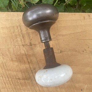May include: Antique door knob with a white porcelain base and a metal top. The metal is rusty and the porcelain is slightly chipped.