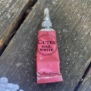 May include: A pink tube of Cutex Nail White nail polish. The tube has a silver cap and is labelled with the brand name and product name.