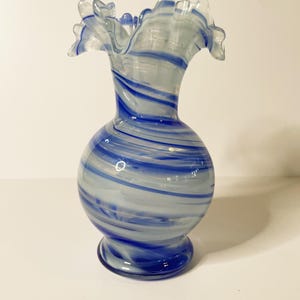 Może przedstawiać: Biały i niebieski szklany wazon o spiralnym wzorze. Wazon ma falbankę na górze i okrągły korpus.