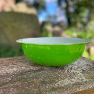 以下が含まれることがあります： 白の内側と緑の外側を持つ緑と白のガラス製のミキシングボウル。ボウルは木製の表面の上に置かれています。