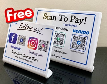 May include: Two white tabletop signs with blue borders. The top sign says "Scan To Pay!" with the text "Touch Free" and has QR codes for Cash App and Venmo. The bottom sign says "Follow us!" with QR codes for Facebook and Instagram. The text "The Cove Custom Signs" and a website address are also on the sign.