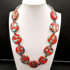 May include: A red, silver, and turquoise necklace with large round beads. The beads have a mosaic-like pattern.