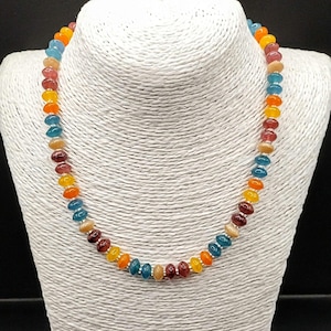 May include: A multi-coloured beaded necklace on a white bust. The necklace is made of gemstone beads in shades of blue, orange, yellow, red, and brown. The beads are strung together with silver-coloured links, creating a vibrant accessory.