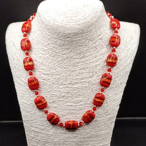 May include: A red and orange glass bead necklace with silver accents. The necklace is on a white mannequin bust.