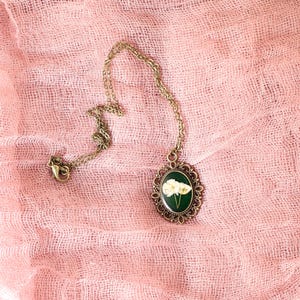 May include: A gold chain necklace with a round pendant featuring a pressed white flower design on a green background.
