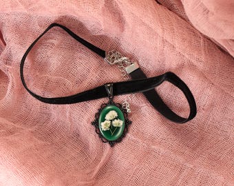 May include: A black velvet choker necklace with a silver chain and a green cameo pendant featuring white pressed flowers.