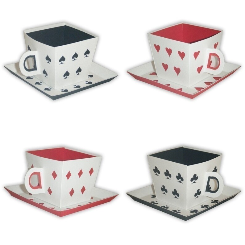 May include: Four white teacups with different playing card suit designs. The cups are made of paper and have a 3D effect. The designs are spades, hearts, diamonds, and clubs.