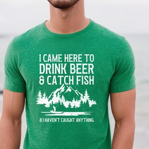 May include: Green t-shirt with a white graphic that says "I came here to drink beer & catch fish. 8 I haven't caught anything". The graphic also includes a silhouette of a person fishing in a lake with mountains and trees in the background.