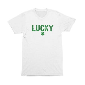 Op de afbeelding: Wit T-shirt met het woord "LUCKY" in groene letters en een groen klavertje vier.