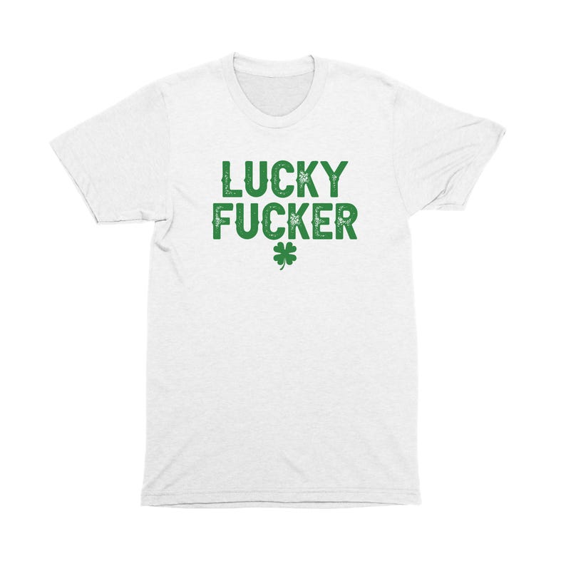 Op de afbeelding: Wit T-shirt met groene tekst die "LUCKY FUCKER" zegt en een groene klaver met vier bladeren.