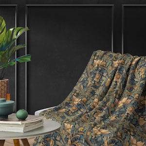 Pode incluir: Uma manta de arremesso azul e dourada com um padrão floral. A manta está drapeada sobre uma cadeira em um quarto com paredes escuras.