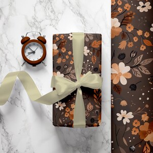 May include: A brown gift box with a floral pattern and a cream-colored ribbon. The box is sitting on a white marble surface with a brown alarm clock next to it.