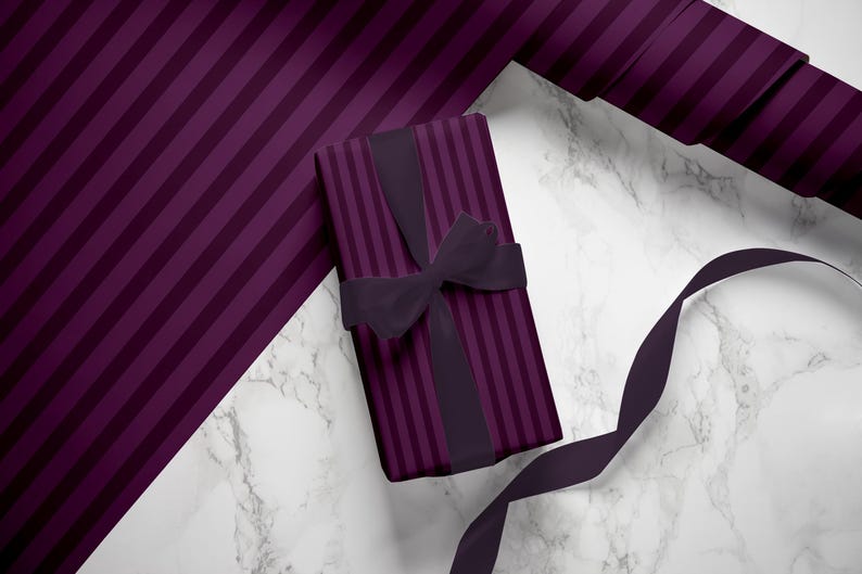 May include: A purple and black striped gift box with a black ribbon and bow. The box is sitting on a white marble surface.