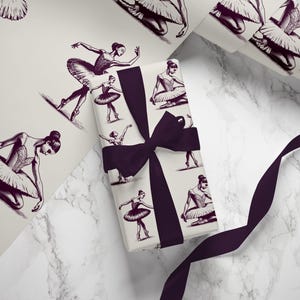 May include: A gift wrapped in white wrapping paper with a purple ribbon. The wrapping paper features a repeating pattern of black and white illustrations of ballerinas in various poses.