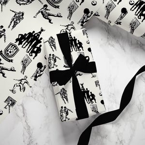 May include: Black and white wrapping paper with a repeating pattern of soccer players, soccer balls, and trophies. The paper is wrapped around a gift box with a black ribbon.