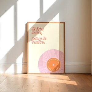 May include: A rectangular framed wall art print featuring a cream-colored background with the text "If it's nice, play it twice." in a pink sans-serif font. Below the text is a stylized illustration of a pink vinyl record with an orange center.