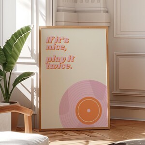 May include: A framed print with a retro design featuring a pink and orange record with the text "If it's nice, play it twice."