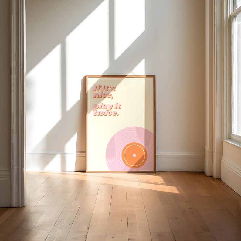 May include: A rectangular framed wall art print featuring a cream-colored background with the text "If it's nice, play it twice." in a pink sans-serif font. Below the text is a stylized illustration of a pink vinyl record with an orange center.