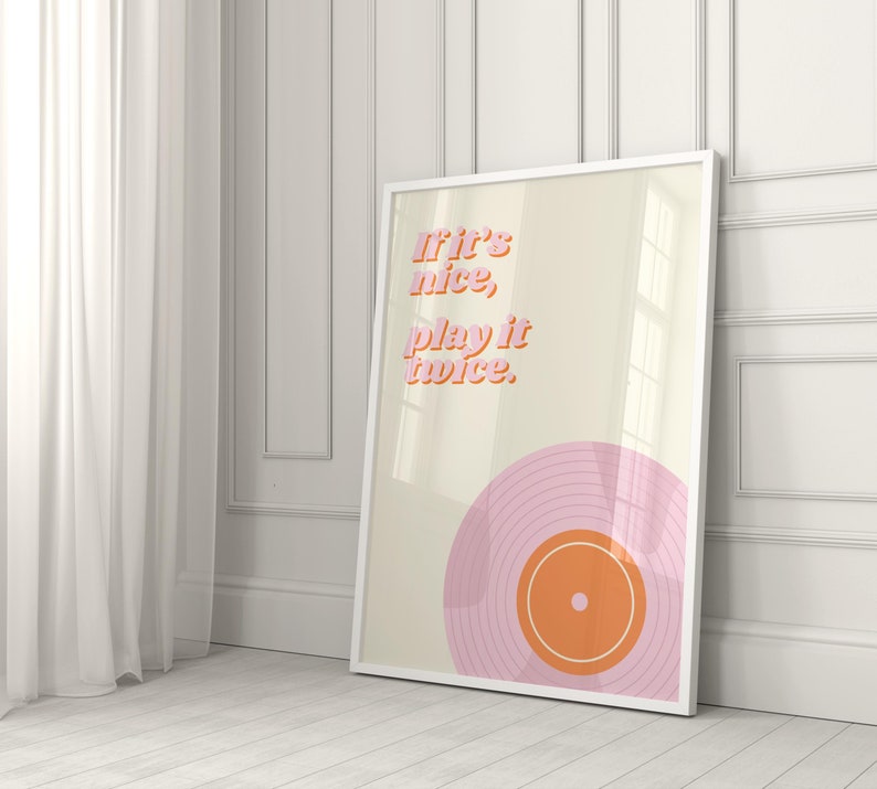 May include: A framed rectangular wall art print featuring a cream background with the pink and orange text "If it's nice, play it twice." Below the text is a graphic illustration of a pink vinyl record with an orange center label and white rings.