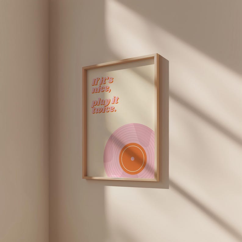 May include: A rectangular framed wall art print featuring a light cream background with the text If it's nice, play it twice in a bold orange font. Below the text is a graphic illustration of a vinyl record in shades of pink and orange.