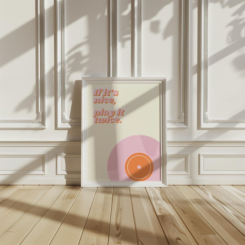 May include: A framed wall art print featuring a cream background with the text 'If it's nice, play it twice.' in a pink and orange font. The bottom right corner displays a stylized graphic of a pink vinyl record with an orange center label.