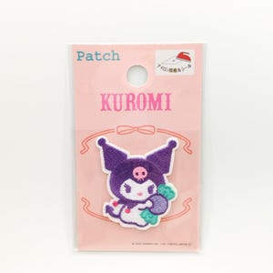 May include: A pink and white packaging card with the text "Patch" and "KUROMI" in black. The card features an embroidered patch of a purple and white cartoon character holding a purple turnip. The text "アイロン接着&シール" is also on the card.