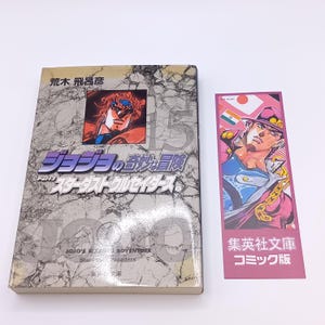 以下が含まれることがあります： キャラクターイラストと日本語のテキストが表紙に描かれた日本の漫画。キャラクターイラストと日本語のテキストが入ったブックマークが本の隣にあります。「JOJO'S Bizarre Adventure」というタイトルの本です。