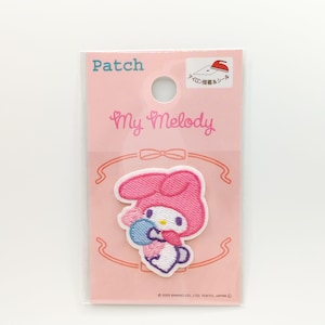 May include: An iron-on patch featuring My Melody, a popular Sanrio character, holding a blue and pink flower. The patch is embroidered in pink and white and is packaged on a pink card with the text "Patch" and "My Melody" in white.