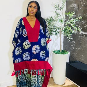 May include: A long, flowing dress with a V-neckline. The dress features a navy blue fabric with a white and yellow circular pattern. It has a red panel at the chest and a red trim with tassels at the hem. The lower portion of the dress has a geometric pattern.
