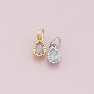 May include: Two teardrop-shaped charms with clear crystal stones set in a gold and silver bezel. The charms have a beaded edge and are perfect for adding a touch of sparkle to jewelry.