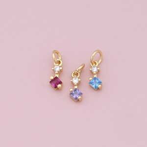 May include: Three gold charms with a small clear gemstone and a larger square gemstone in pink, blue, and purple.