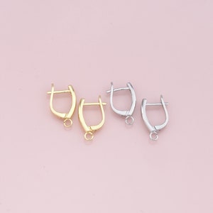 May include: Two pairs of earring findings, one pair is gold and the other is silver. The findings are shaped like a small hoop with a loop at the bottom.