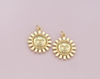 May include: Two gold sun charms with a face design. The charms are on a pink background.