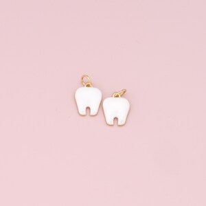 May include: Two white tooth charms with gold loops. The charms are shaped like teeth and have a smooth, white finish.