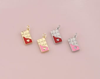 Può includere: Quattro piccoli ciondoli a forma di barretta di cioccolato. Due sono dorati e due argentati. Ogni ciondolo ha una forma rettangolare con un motivo a griglia e un design a forma di cuore in smalto rosso o rosa. Su sfondo rosa.