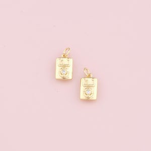 May include: Two gold-tone charms shaped like vintage cassette tapes with a single clear rhinestone on each.