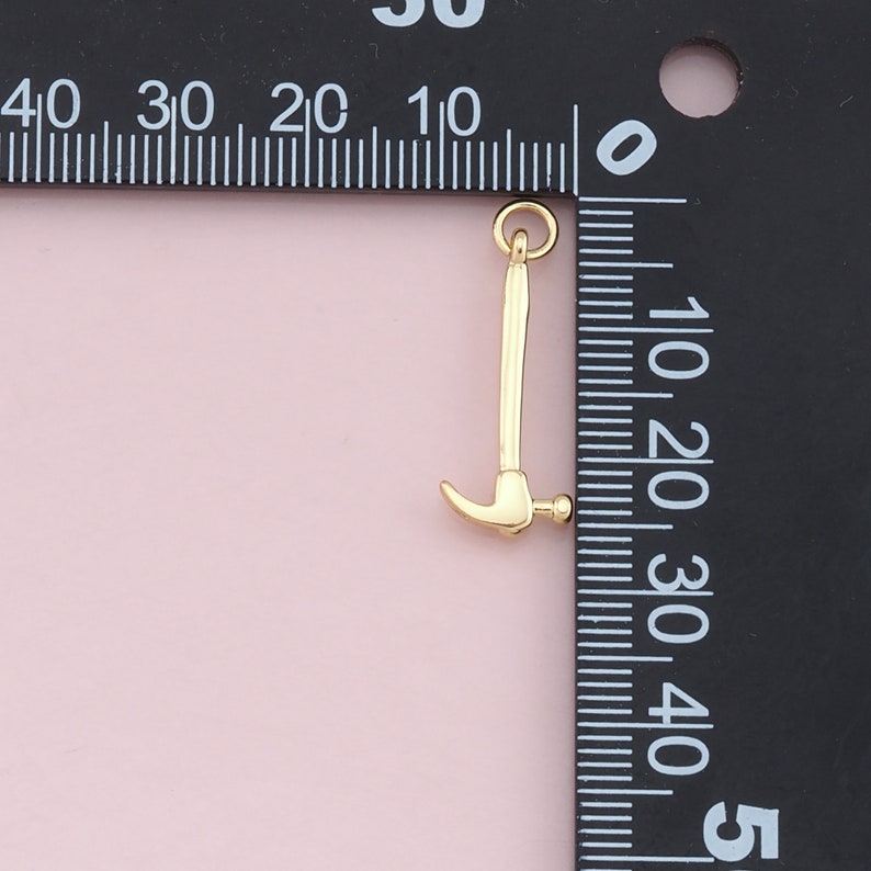 May include: A gold-colored hammer charm with a loop at the top for attaching to a necklace or bracelet.
