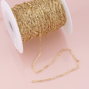May include: A spool of gold-coloured chain, with a length of the chain laid out on a pink surface.