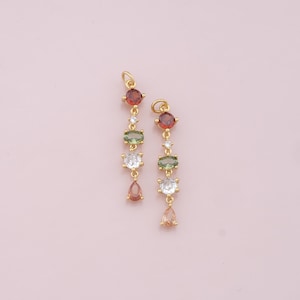 May include: A pair of gold dangle earrings with a teardrop-shaped stone at the bottom and a series of round and oval-shaped stones in red, green, and white.