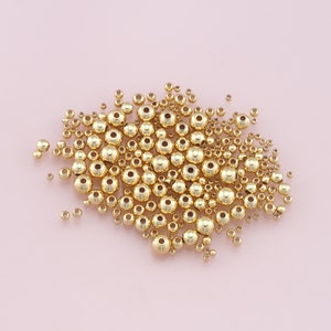 May include: A large pile of gold-colored round beads, scattered on a pink surface.