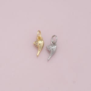 May include: Two shell charms, one gold and one silver, with clear crystal accents. The charms are shaped like a seashell with a pointed tip.