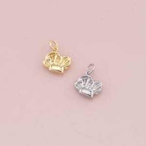 May include: Two chef hat charms, one gold and one silver, on a pink background.