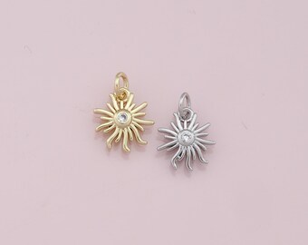 May include: Two sun charm pendants with a small clear rhinestone in the center. The charm on the left is gold and the charm on the right is silver.