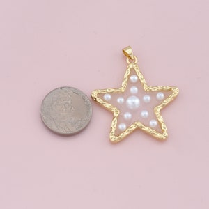 Pu&ograve; includere: Ciondolo a forma di stella color oro con bordo strutturato, riempito di perle bianche. Il ciondolo &egrave; accanto a una moneta per il confronto delle dimensioni. La stella ha un piccolo anello nella parte superiore.